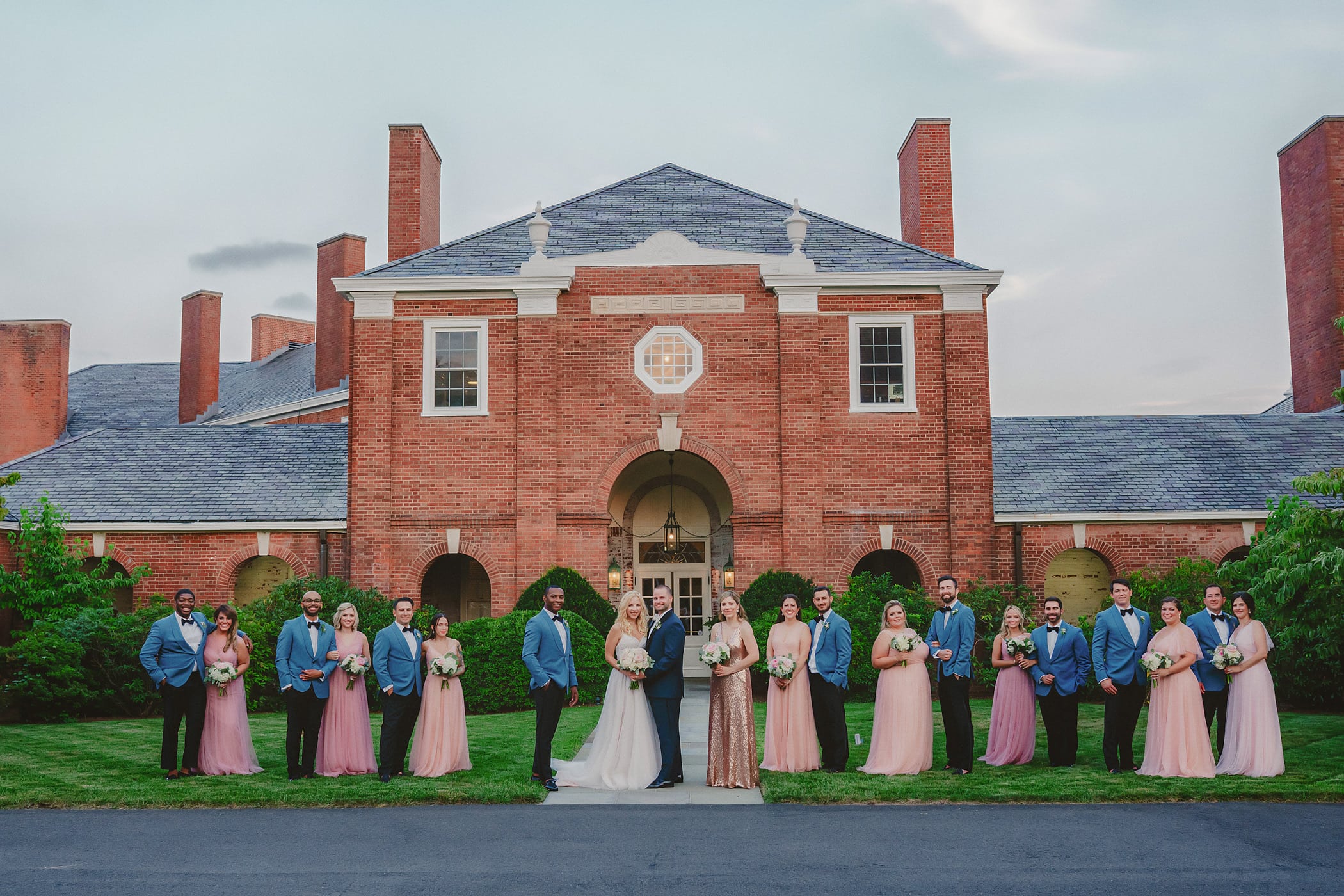 Photo of a large bridal party where bride's maids are wearing pink dresses and groomsman blue suits